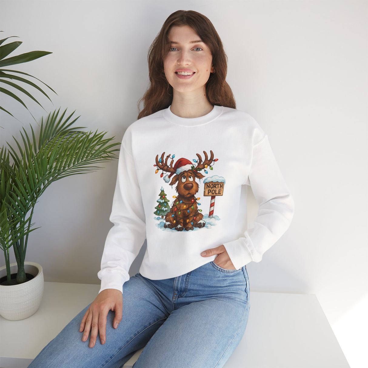 Cozy Christmas Moose Crewneck Sweatshirt showing a fun design of a reindeer by a tiny decorated tree.